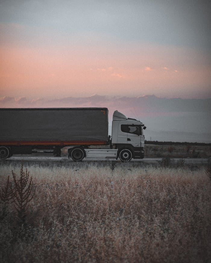 A cargo truck travels on a highway at sunset, surrounded by an open landscape, symbolizing logistics and transportation.